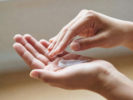 Close-up of hands warming a small amount of unbranded moisturizer in soft natural daylight